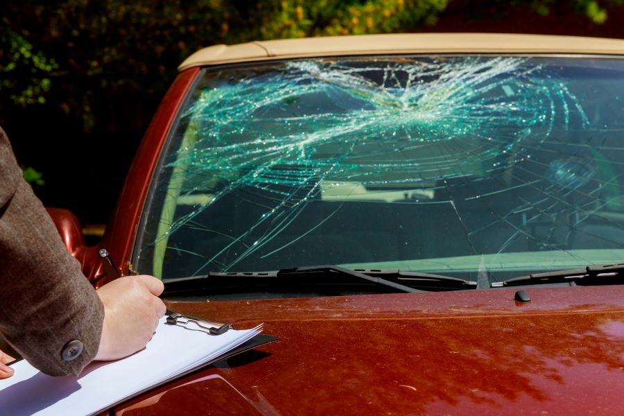 a man with a clipboard writing on the hood of a car with smashed windshield