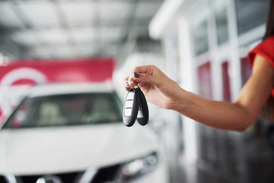 a hand holding a set of car keys with a blurred image of a car in the background