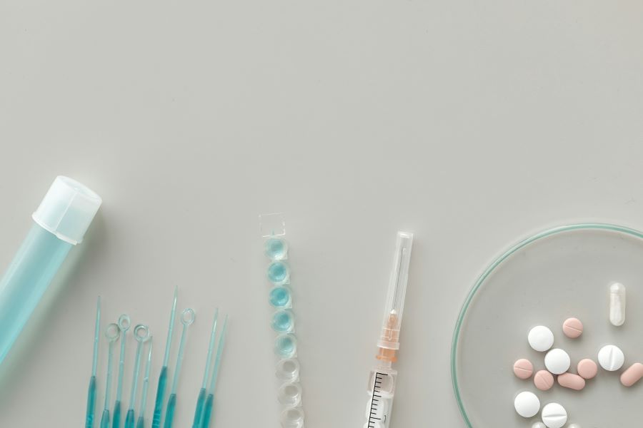 neutral background with pills, a syringe, a vial and medical tools