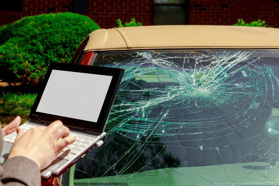a person typing on a small laptop with a car with smashed windshield in the background