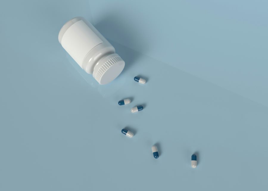 a prescription bottle and white and blue pills on light blue background