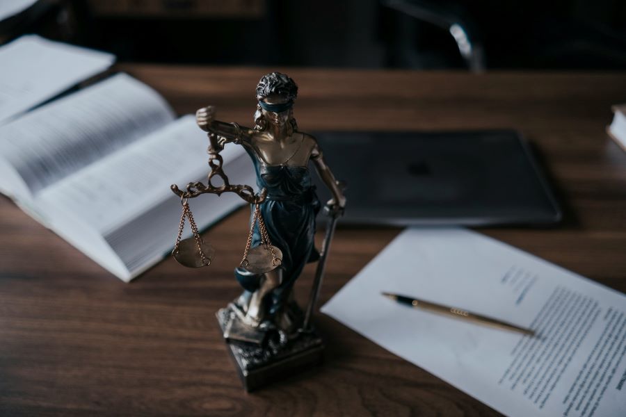 a statue of themis in front of a book and a paper with pen laying on it