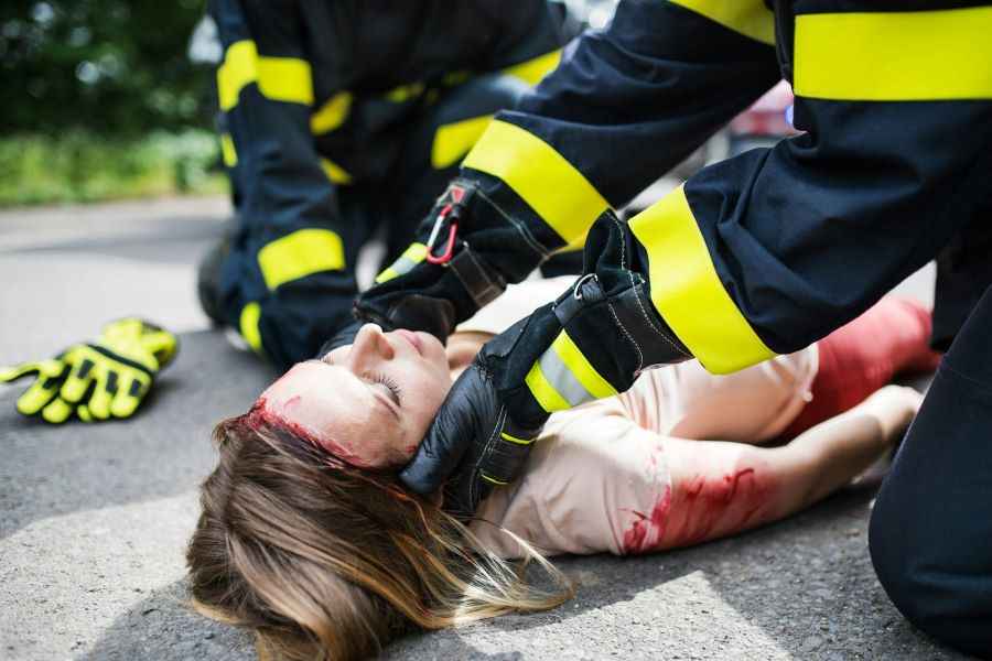 a bleeding, injured woman lying on the ground while paramedics attend to her