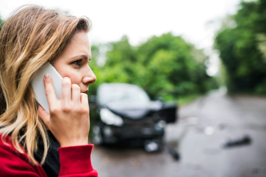 a woman on a cell phone with a wrecked car in the background