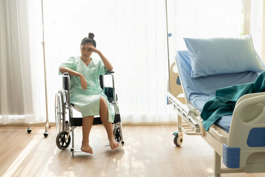 a woman in a wheelchair next to a hospital bed is holding her head in her hand