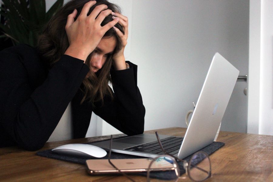 a woman clutches her head while looking at laptop display