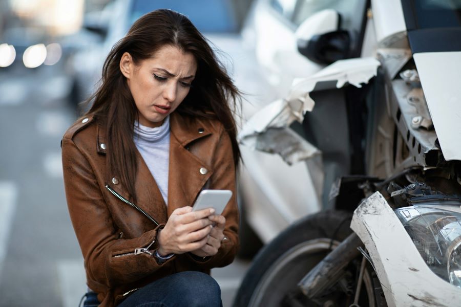 a woman looking at her phone next to a wrecked car
